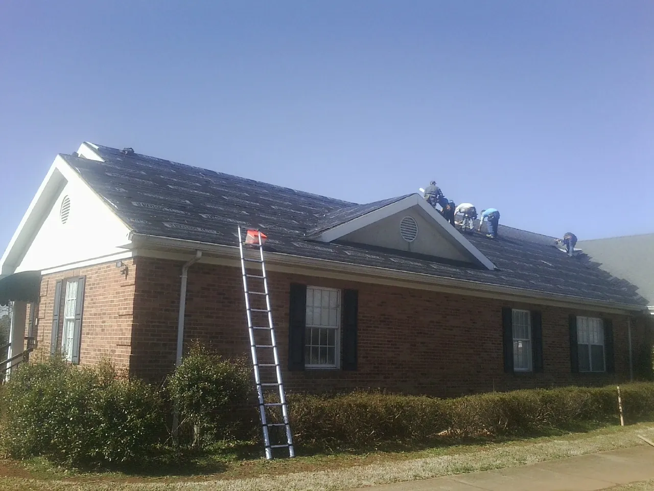 Crew tearing shingles off a brick ranch roof with a ladder set — Emergency Roof Repair work by our crew in Hannibal