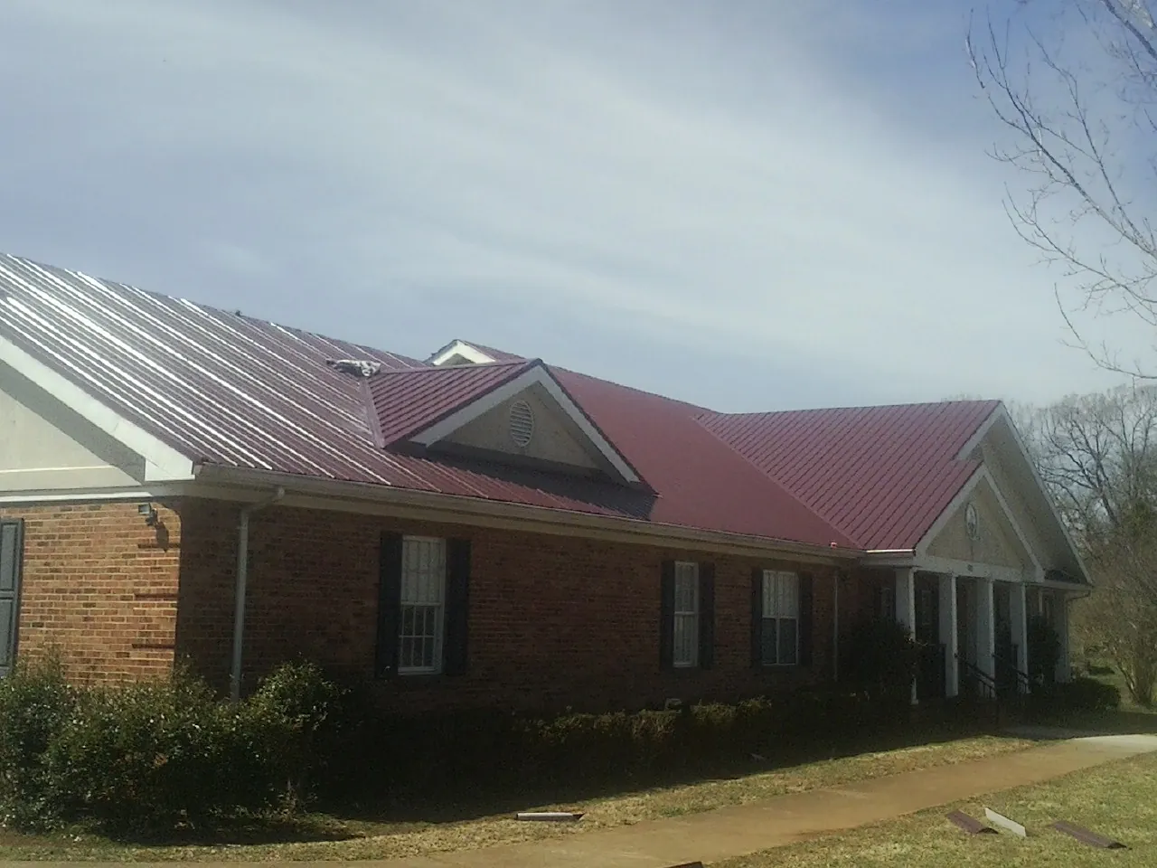 Red metal roof with gabled entries on a long brick building, from a Hail Damage Roof Repair job in Hannibal
