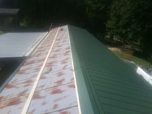 Old rusted panels beside newly installed green metal roofing — Wind Damage Roof Repair by Roofing Brothers in Hannibal