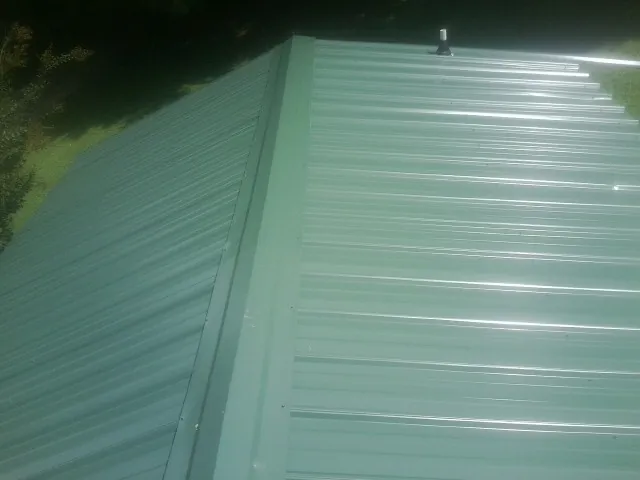 New green metal panels meeting at the ridge of a roof — Flat Roof Repair work by our crew in Hannibal